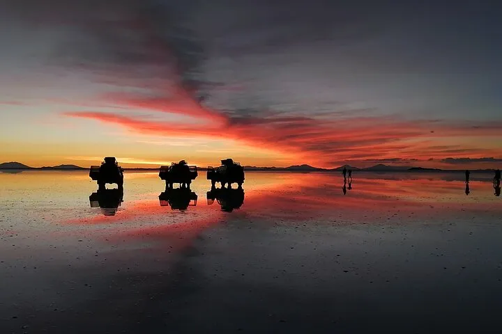 Tourists wading in shallow water for the mirror effect on a Uyuni salt flats tour at sunset