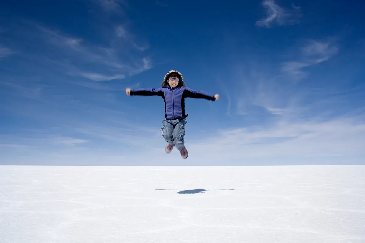A traveller jumping over the flat white salar for a perspective photo on an Uyuni salt flats tour